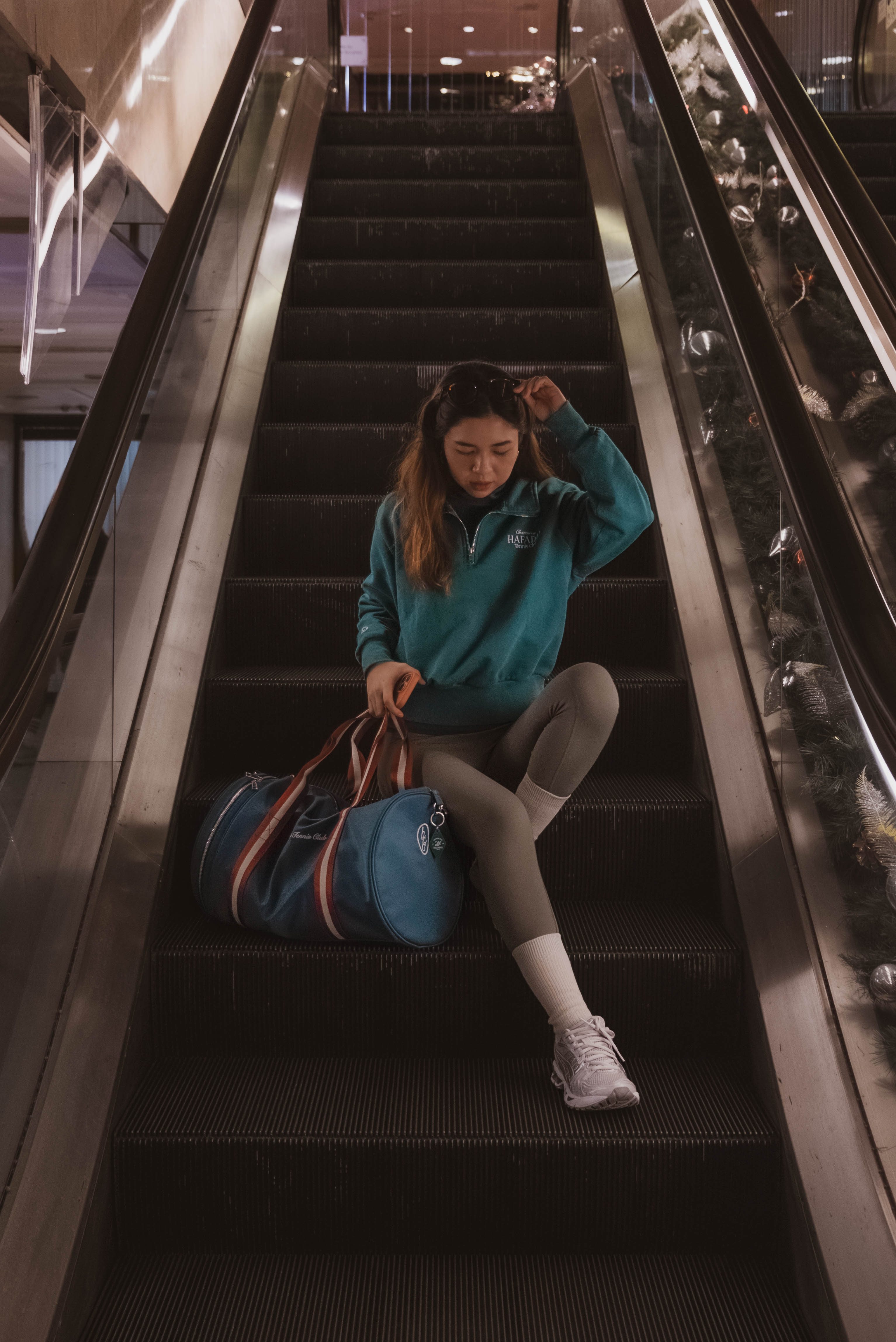 Person sitting on an escalator with a blue bag