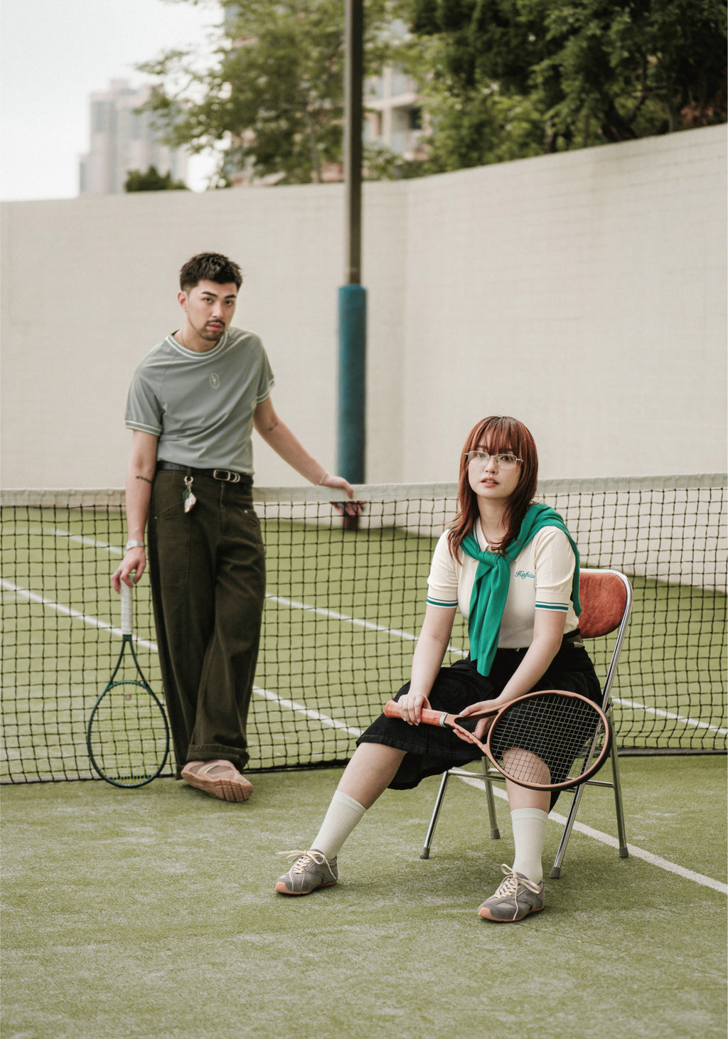 Two people on a tennis court with tennis rackets, one standing and one sitting.