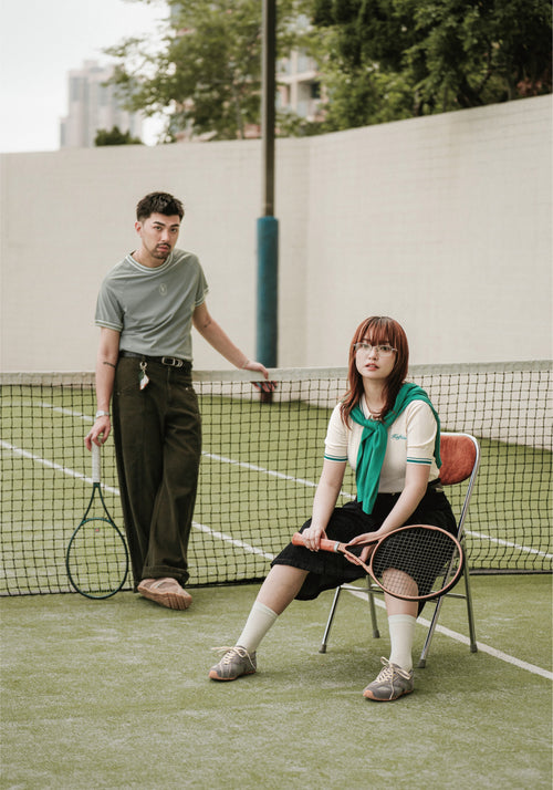 Two people on a tennis court with tennis rackets, one standing and one sitting.